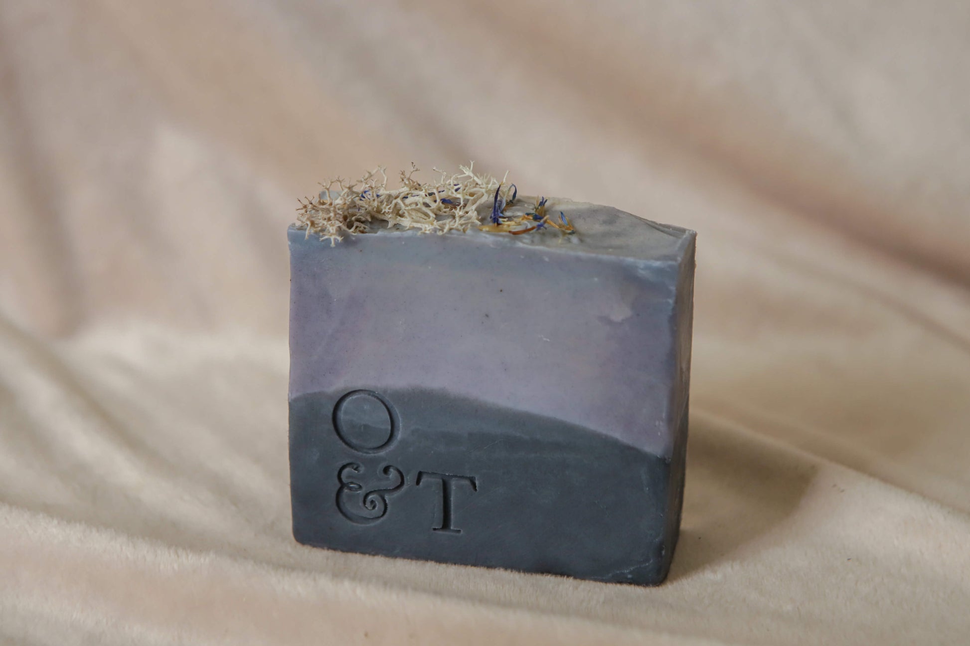 Large moss soap bar, light grey blue black base with a deep mid but top decorated with corn flower petals and soft white reindeer moss, stamped with the o&t logo